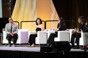 Aurora's CEO Virgel Hammonds sits on stage moderating a panel of student presenters. He sits in a chair across from four students, each seated in their own chair.